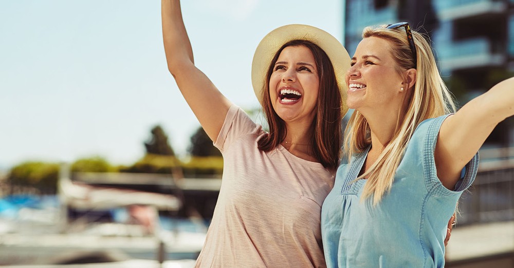 Two female friends standing arm in arm while having a good time together in the city in summer.